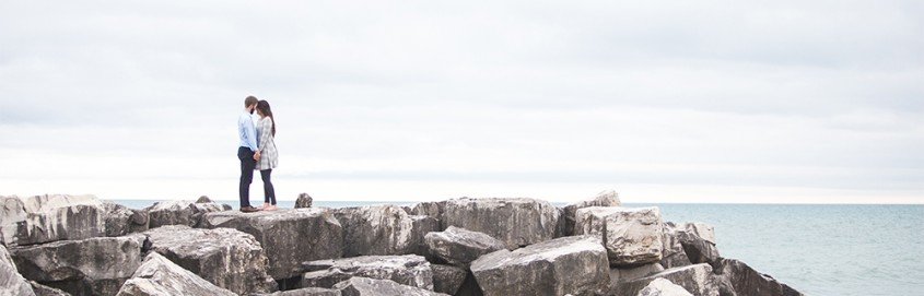 Couple standing on rocks over water.