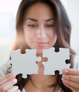 young woman holding two puzzle pieces in front of her face. 